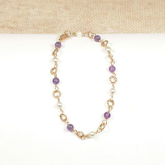 A 9ct gold bracelet with round cabochon amethyst stones and matching cultured pearls, featuring a fine gold rope threading and a gold lobster clasp, displayed against a beige background.