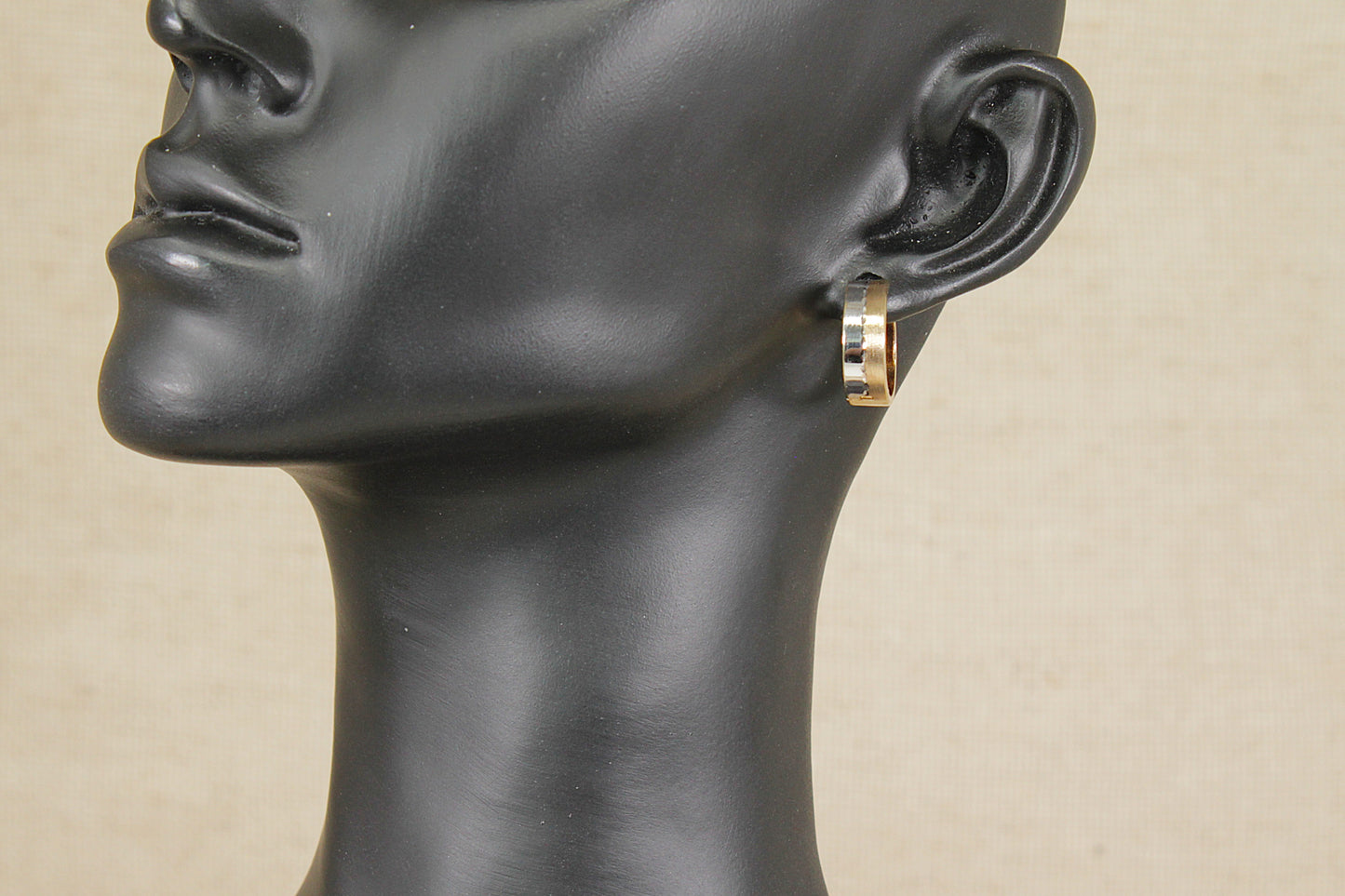Mannequin head with a gold hoop earring on a beige background