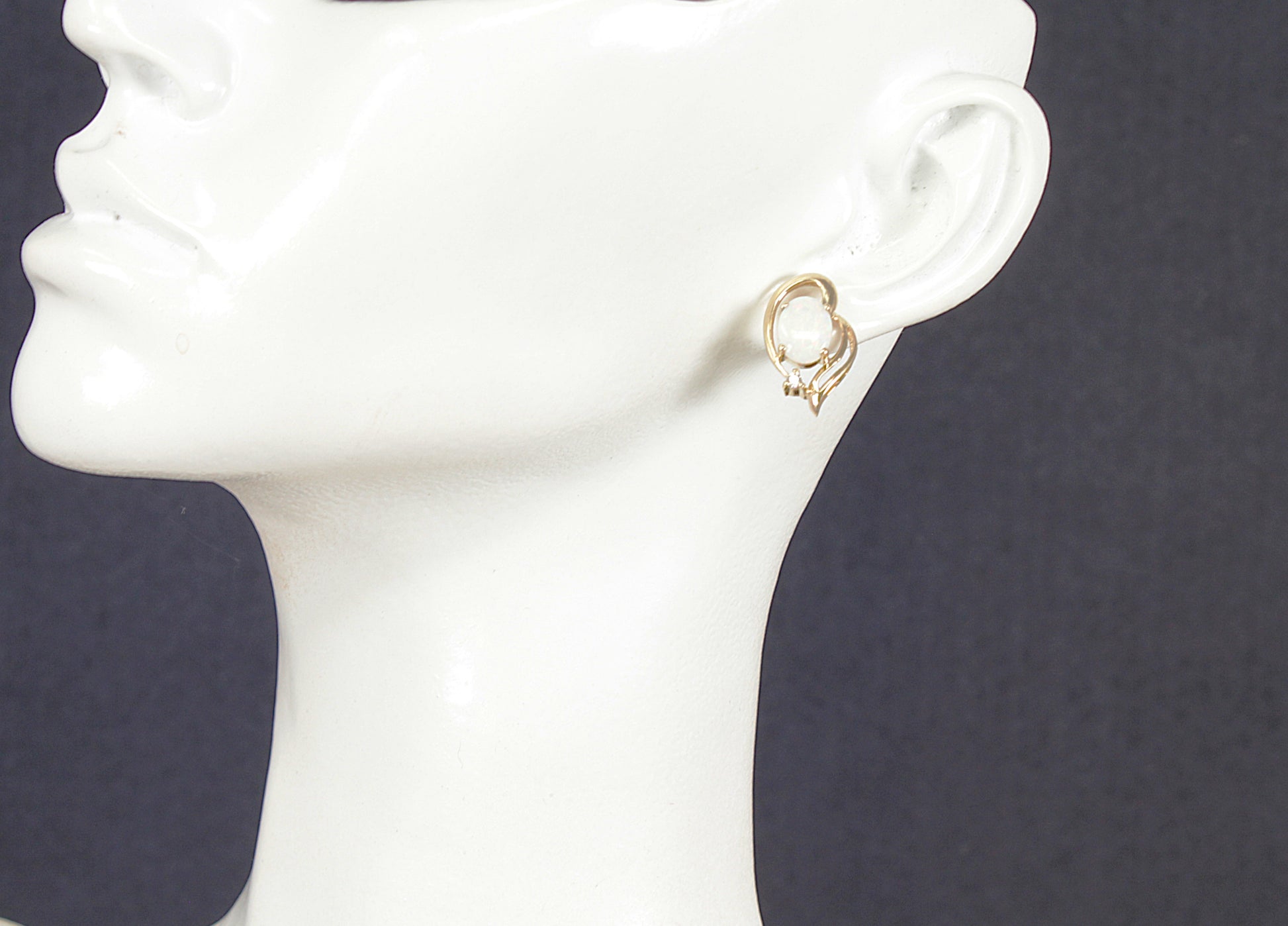 Gold opal stud earrings on a white mannequin head against a dark background