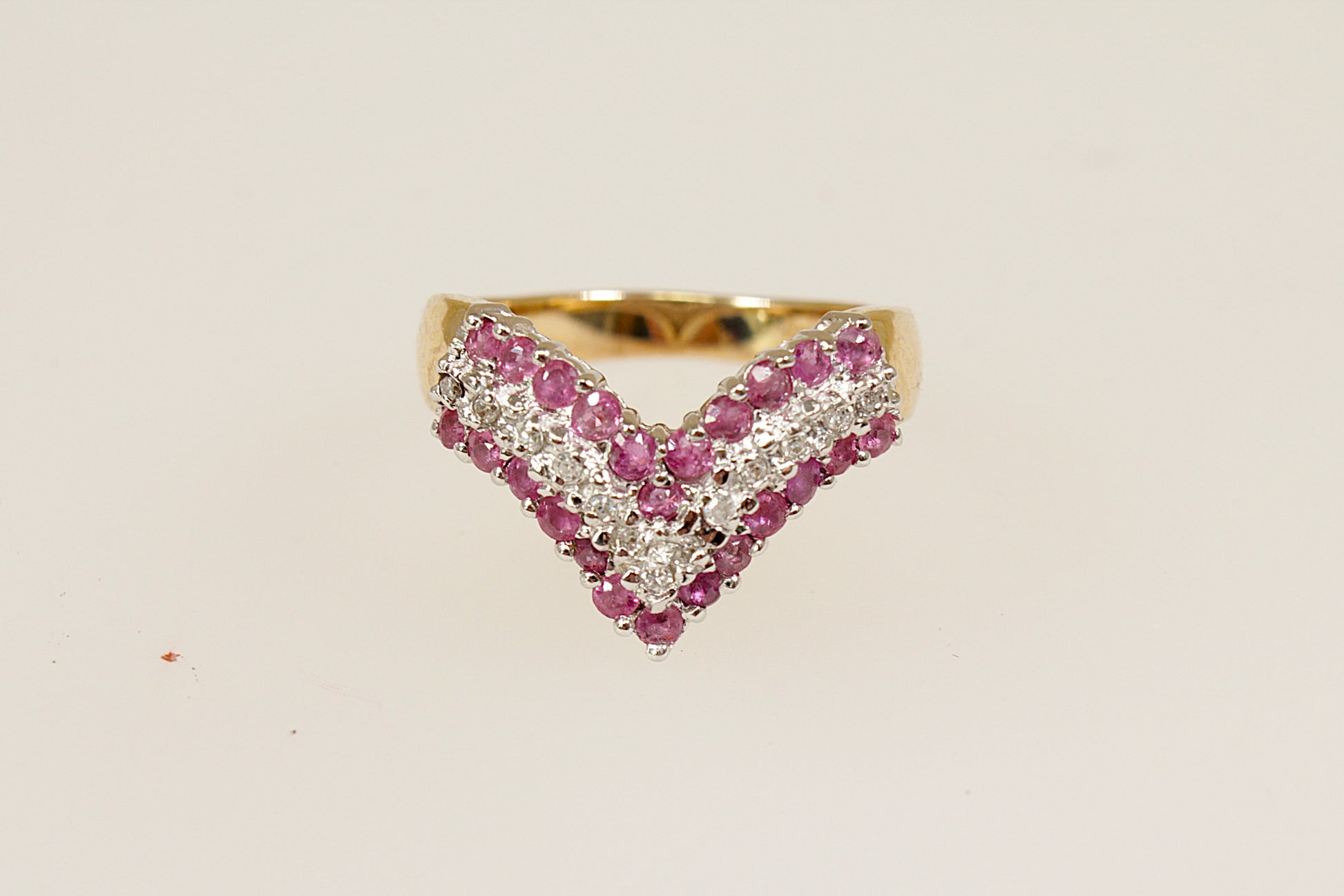 This beautiful 9ct Gold cluster ring is designed in a wishbone shape; featuring 3 bands of gemstones, creating a striking and meaningful design. The two rows of round-cut rubies (24 in total) bring a vibrant deep red colour, symbolising passion and prosperity, while the central row of diamonds adds a touch of brilliance and contrast, enhancing the overall sparkle. The London hallmarks for 1992, UK finger size M.
