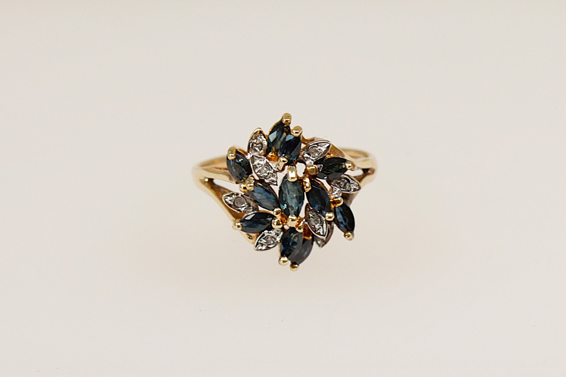 This 9ct Gold ring is a breathtaking and artistic statement piece! This large Sapphire and Diamond flower design ring features 11 Marquise-cut blue Sapphires in claw settings and 8 round diamond accents, Birmingham hallmarks for year 1994 and stamped DIA. UK finger size O. 