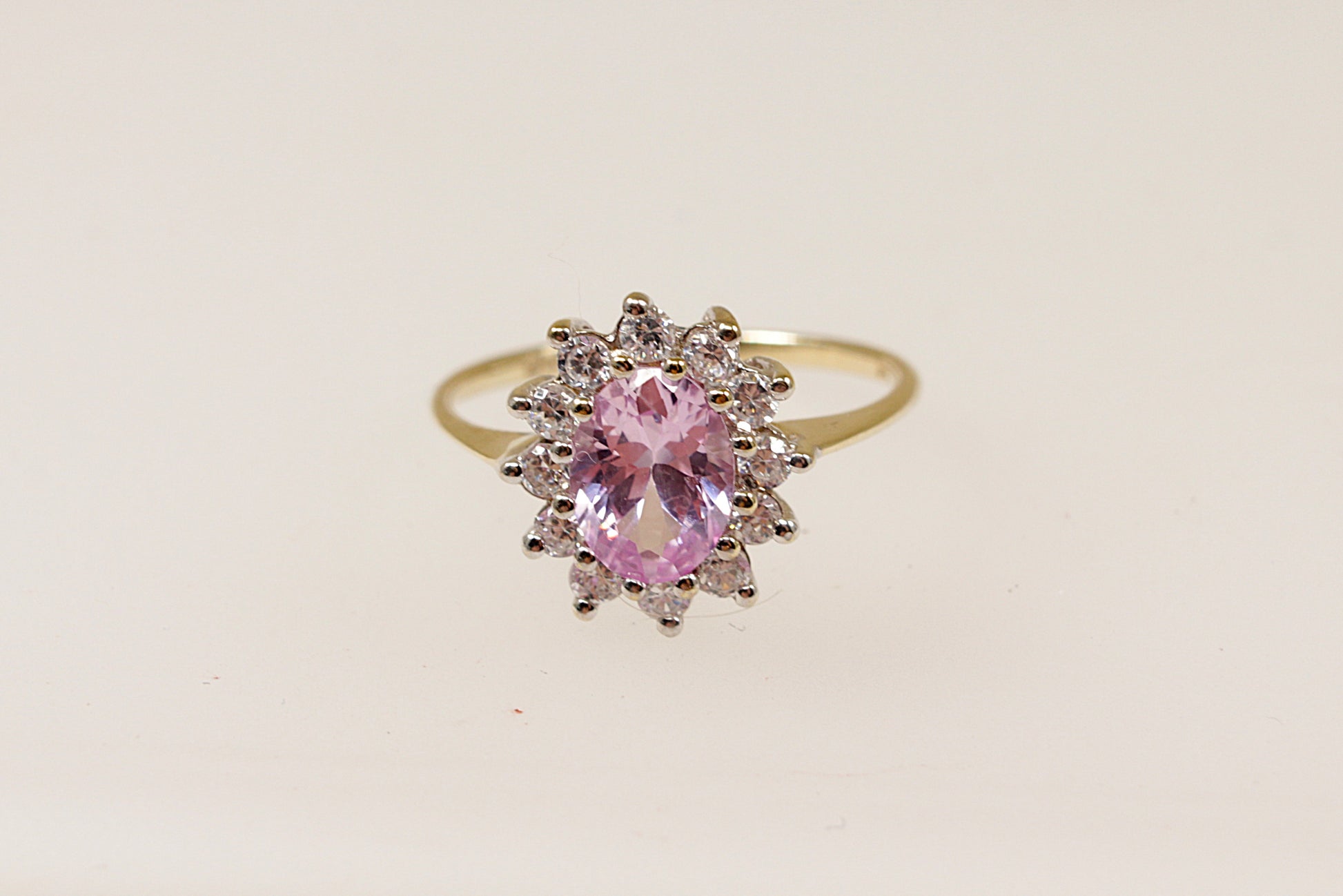 A 9ct gold ring with an oval pink sapphire centerpiece and a halo of round-cut cubic zirconia around it.