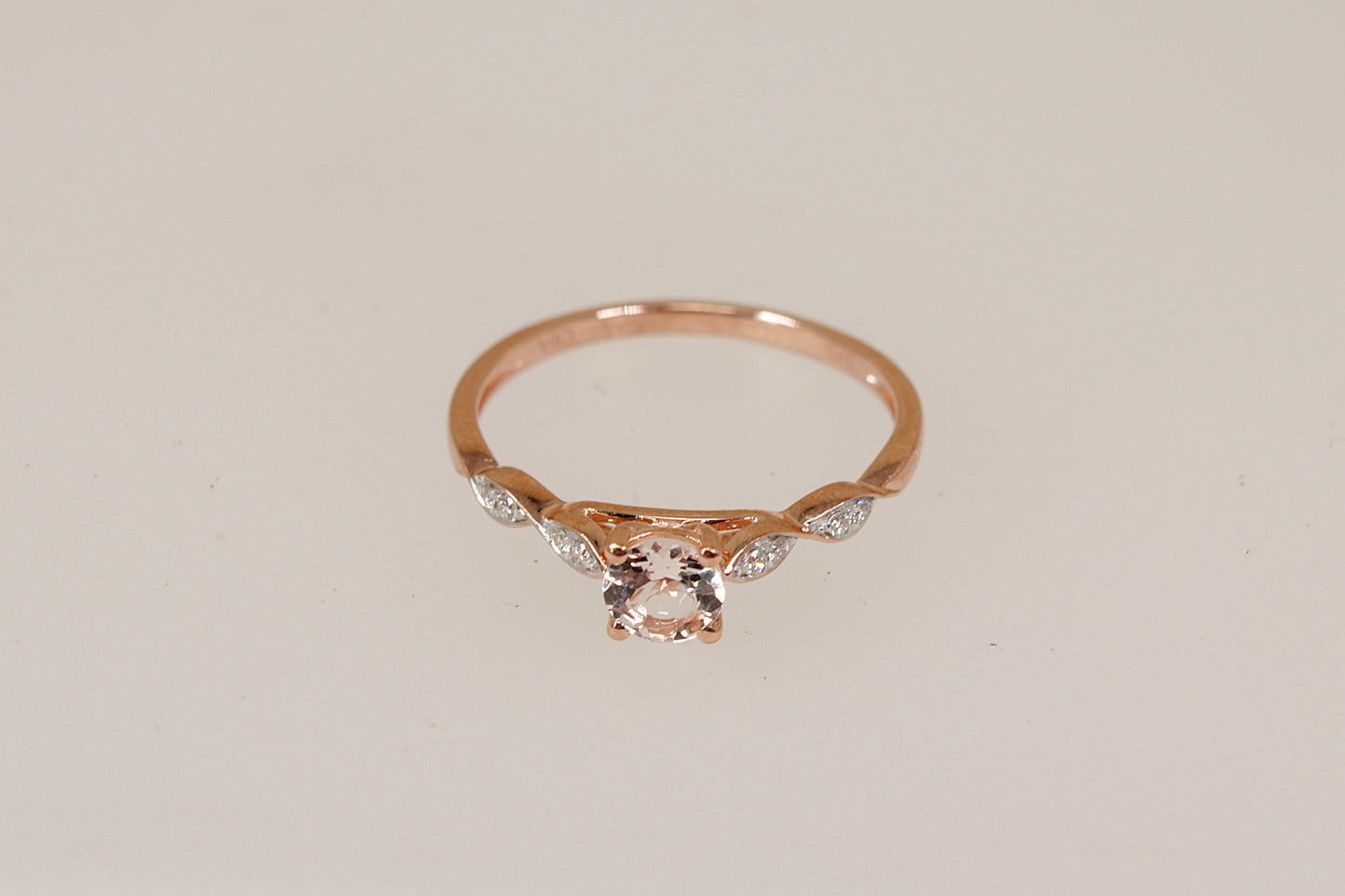Rose gold ring with a central morganite gemstone and smaller diamond gemstones on a light beige background