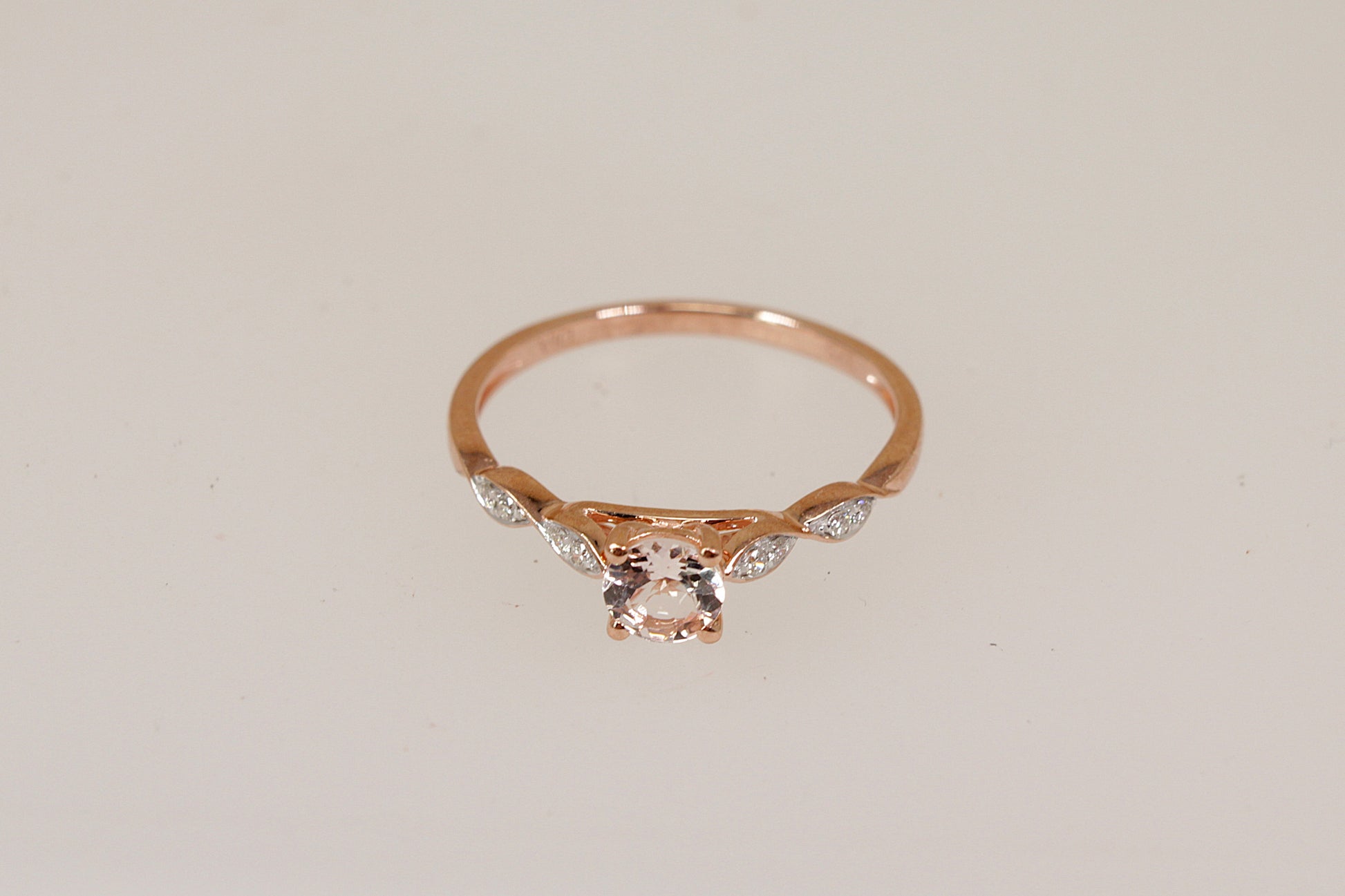 Rose gold ring with a central morganite gemstone and smaller diamond gemstones on a light beige background