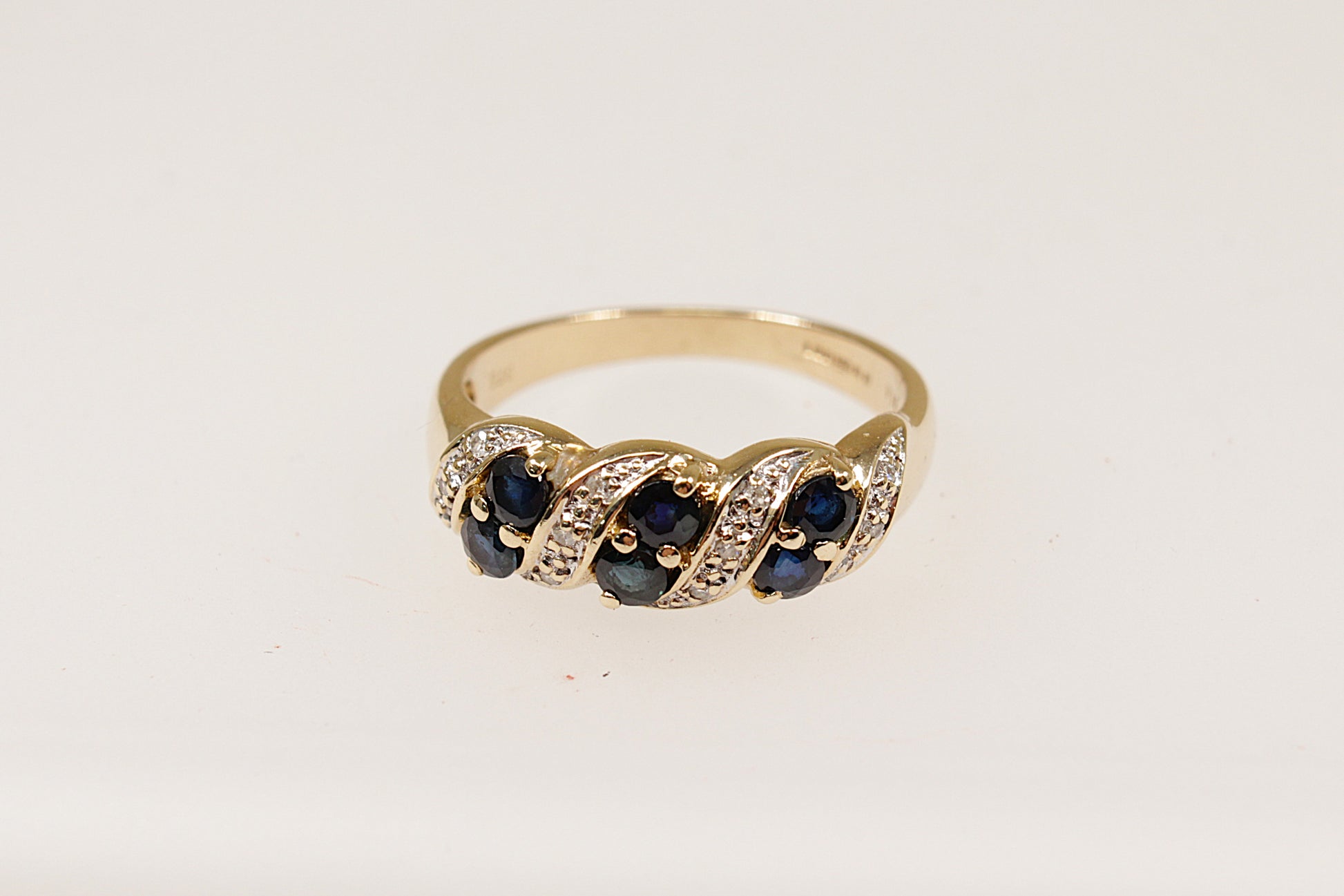 A 9ct gold ring featuring a slanted arrangement of round sapphires with diamond accents, claw set on the band.