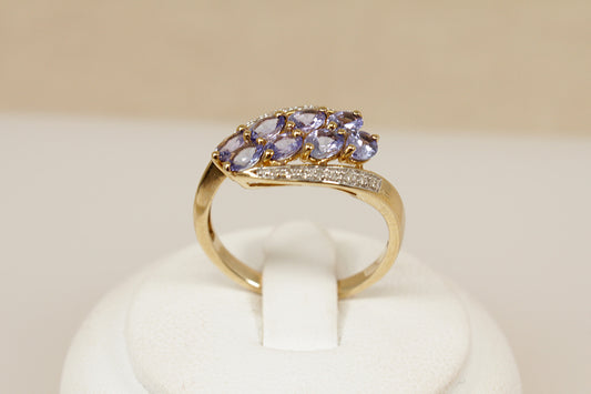 Gold ring with blue tanzanite gemstones on a white stand against a beige background