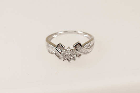 A white gold diamond cluster ring with a floral-inspired design, featuring a flower-shaped crown setting with nine petite diamonds, and baguette-cut diamonds on the shoulders.
