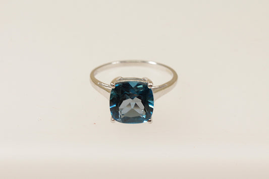 A 9ct white gold solitaire ring with a cushion cut London Blue Topaz held securely in a crown setting with four claws.