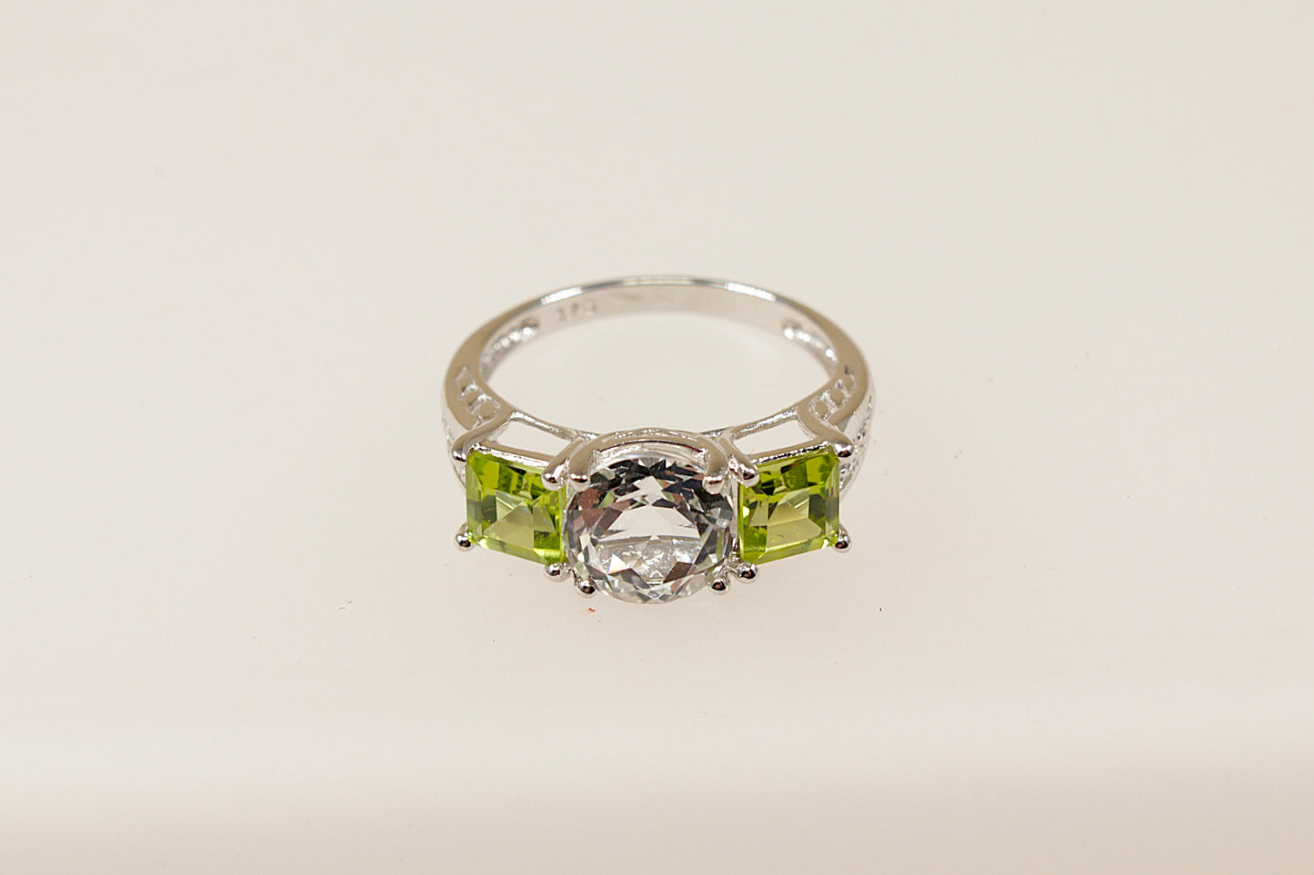 A 9ct white gold trilogy ring with a round white topaz centerpiece and square-cut peridot side stones on a white background.