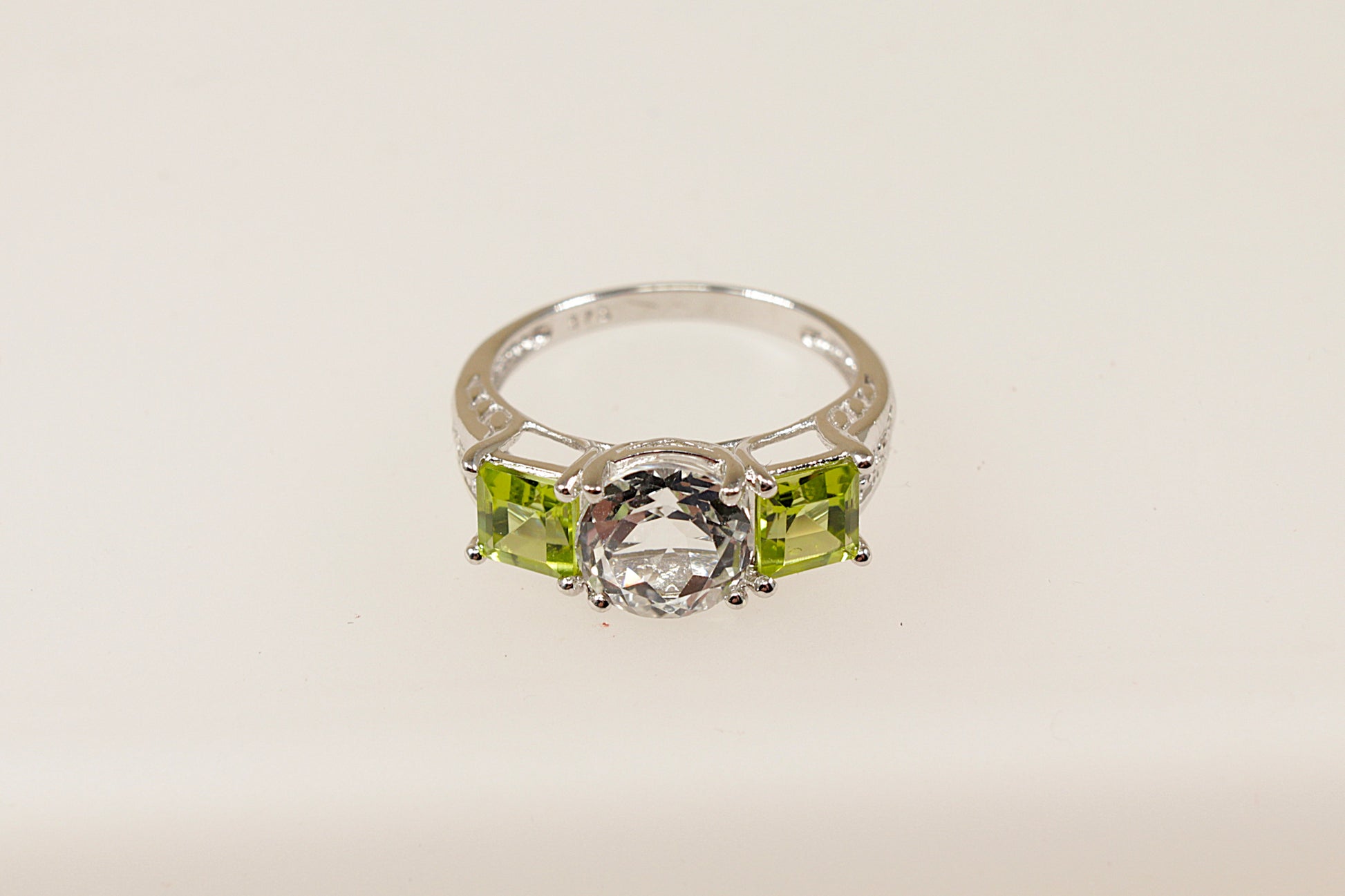 A 9ct white gold trilogy ring with a round white topaz centerpiece and square-cut peridot side stones on a white background.