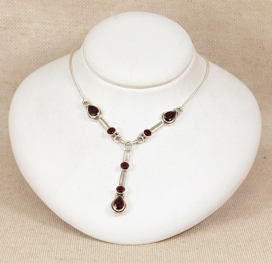 Silver necklace with red garnet gemstones on a white stand against a beige background