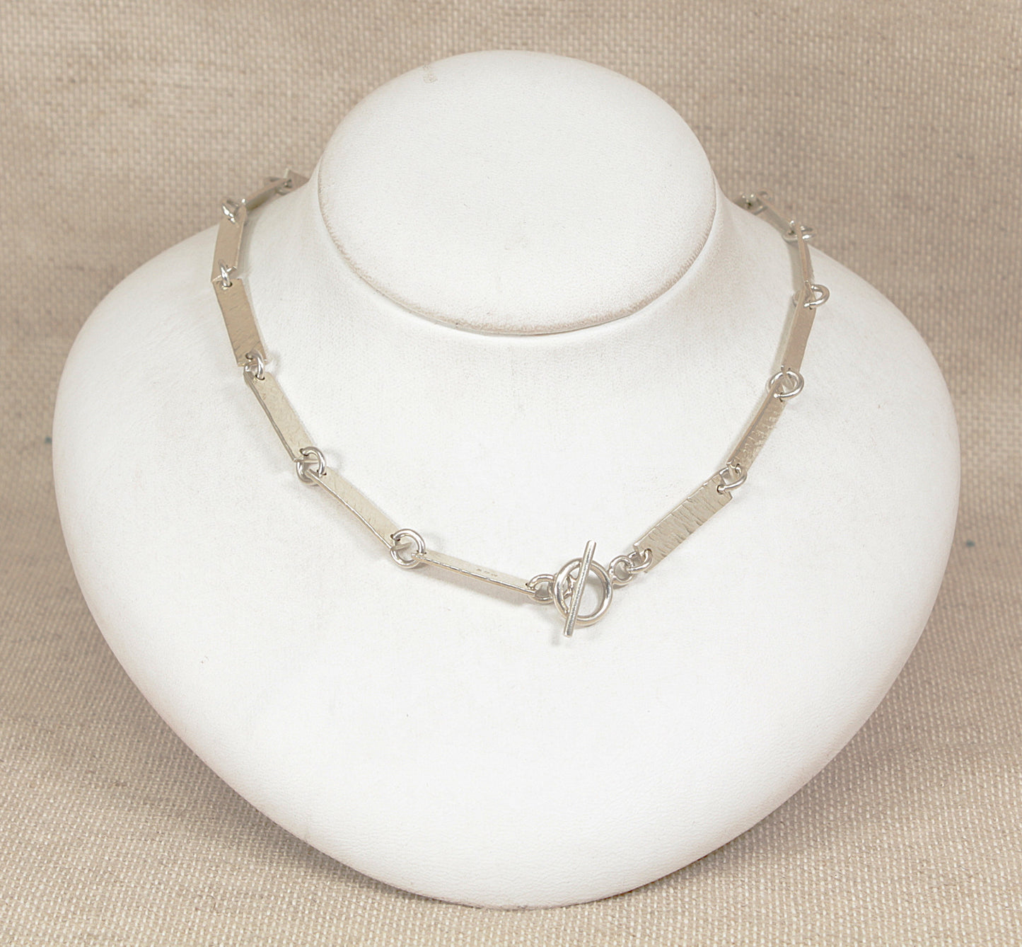 Silver necklace on a white mannequin bust against a beige background
