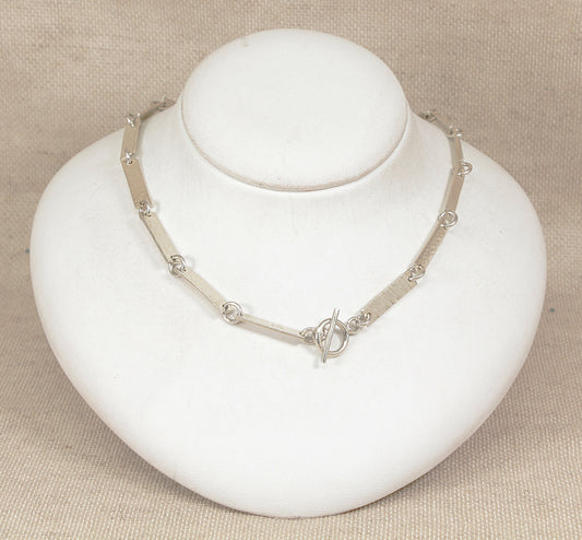 Silver necklace on a white mannequin bust against a beige background