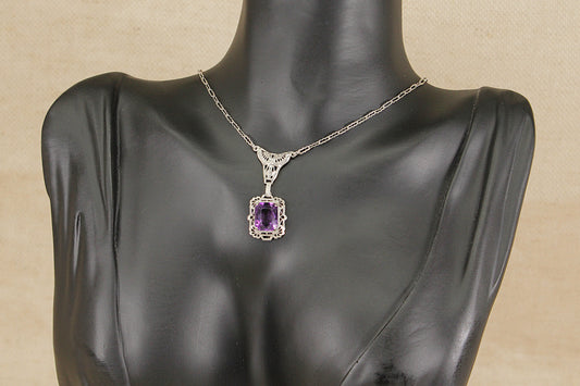 Vintage silver necklace with a purple amethyst gemstone pendant on a mannequin bust against a beige background