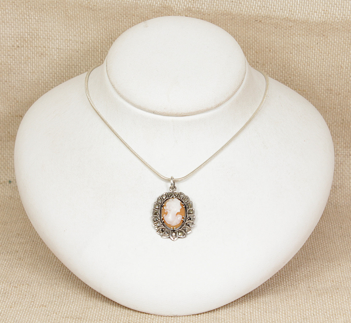 Silver necklace with a cameo pendant on a white stand against a beige background