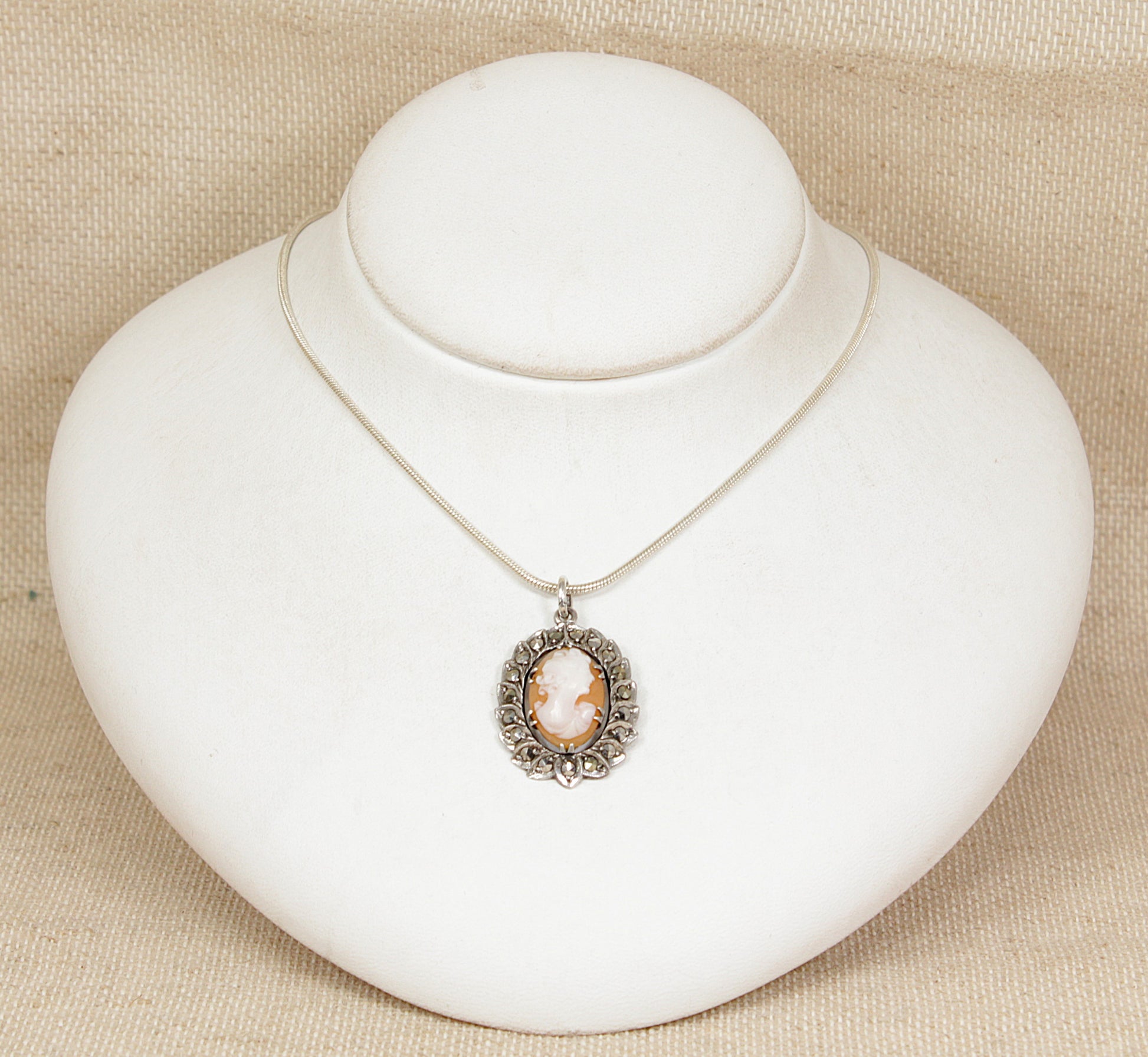Silver necklace with a cameo pendant on a white stand against a beige background