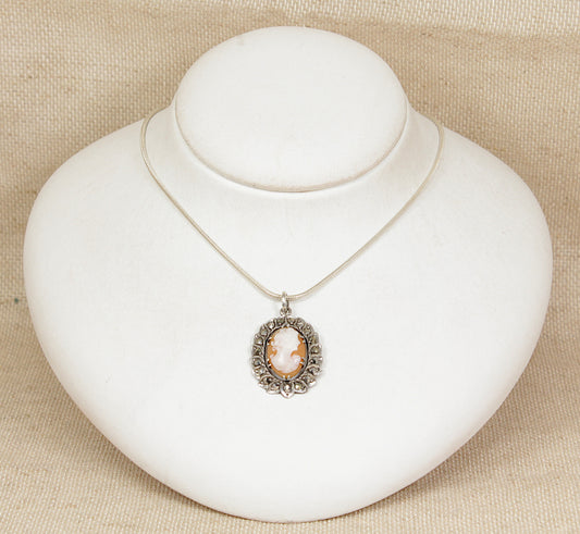 Silver necklace with a cameo pendant on a white stand against a beige background