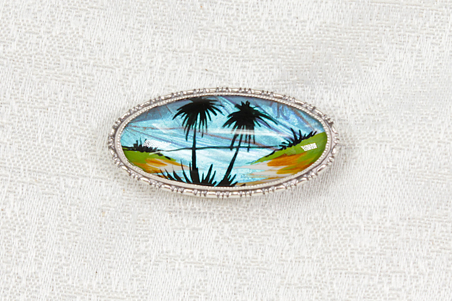 Silver brooch with palm trees design on a white background 
