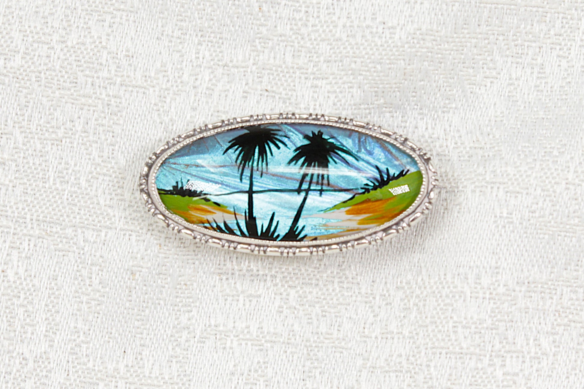 Silver brooch with palm trees design on a white background 