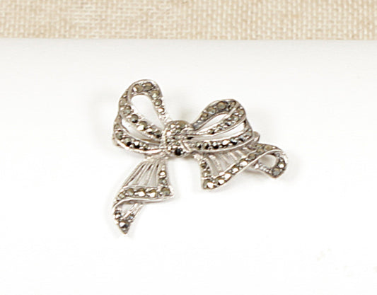 This charming Art Deco Silver and marcasite brooch is an elegant piece! The swirly bow design reflects the graceful curves and geometric influences typical of the Art Deco era, which often combined femininity with bold styling. It is in great condition, has a secure roll over C clasp and stamped SILVER.