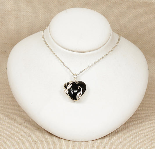 Art nouveau heart-shaped silver and onyx pendant necklace on a white stand with a beige background