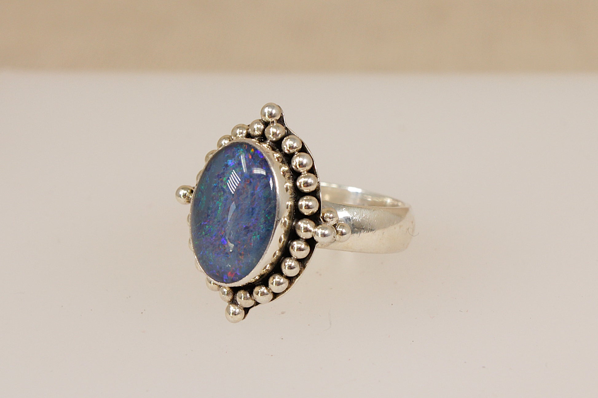 Silver Suarti designer ring with a blue opal gemstone on a beige background