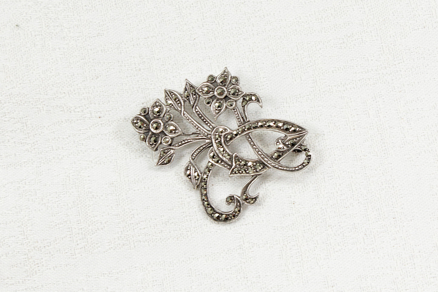 Silver and marcasite brooch with intricate design on a white background