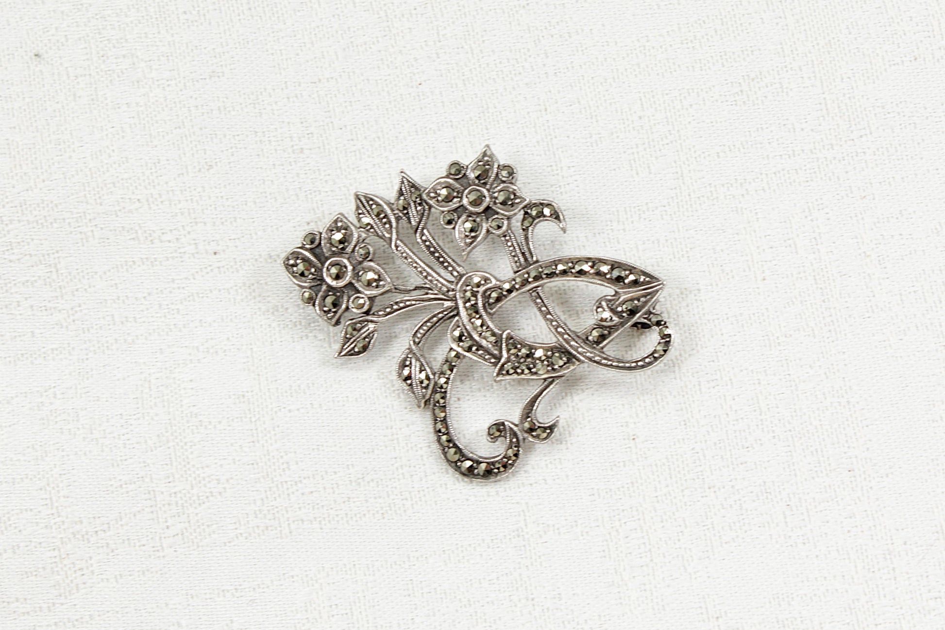 Silver and marcasite brooch with intricate design on a white background