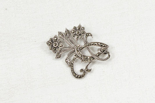 Silver and marcasite brooch with intricate design on a white background