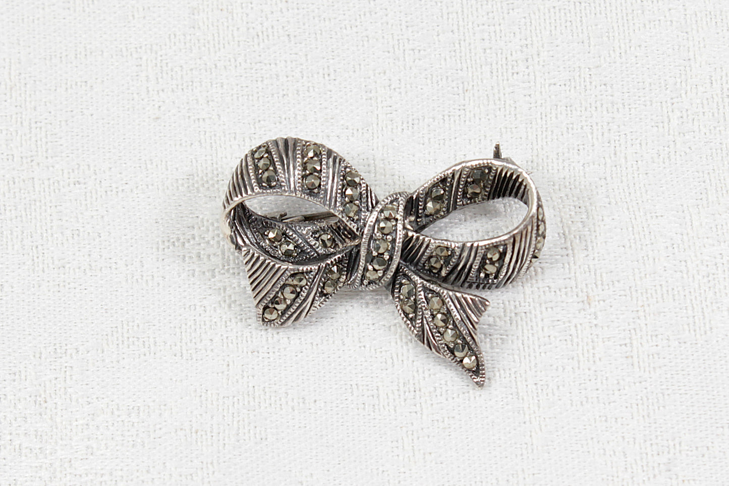 Silver bow-shaped brooch with marcasite stones on a white fabric background