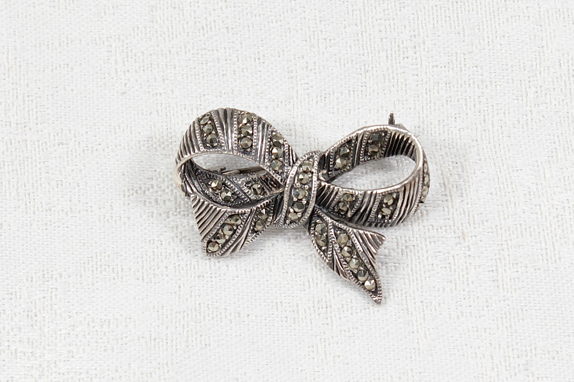 Silver bow-shaped brooch with marcasite stones on a white fabric background