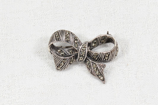 Silver bow-shaped brooch with marcasite stones on a white fabric background