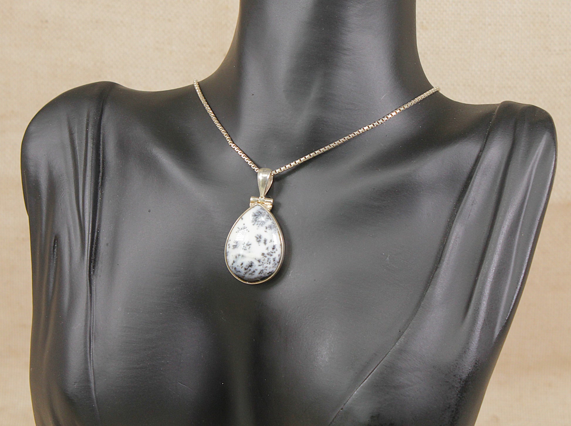 Teardrop-shaped moss agate pendant necklace on a black mannequin bust against a beige background