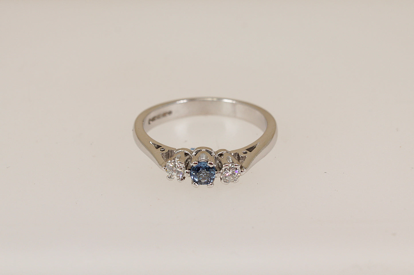 18ct white gold ring with a blue sapphire gemstone and two smaller diamond gemstones on a light beige background