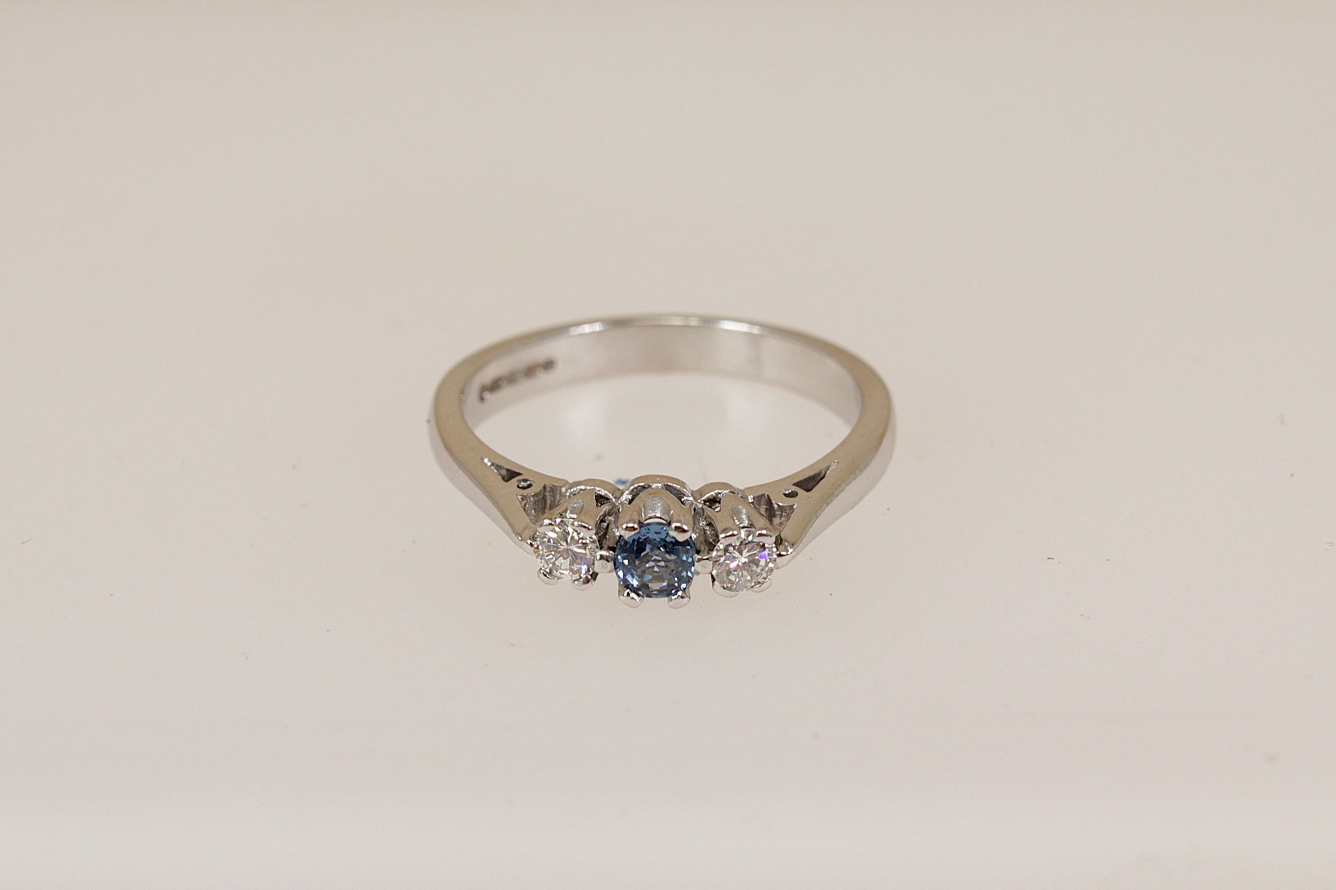 18ct white gold ring with a blue sapphire gemstone and two smaller diamond gemstones on a light beige background