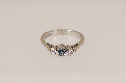 18ct white gold ring with a blue sapphire gemstone and two smaller diamond gemstones on a light beige background