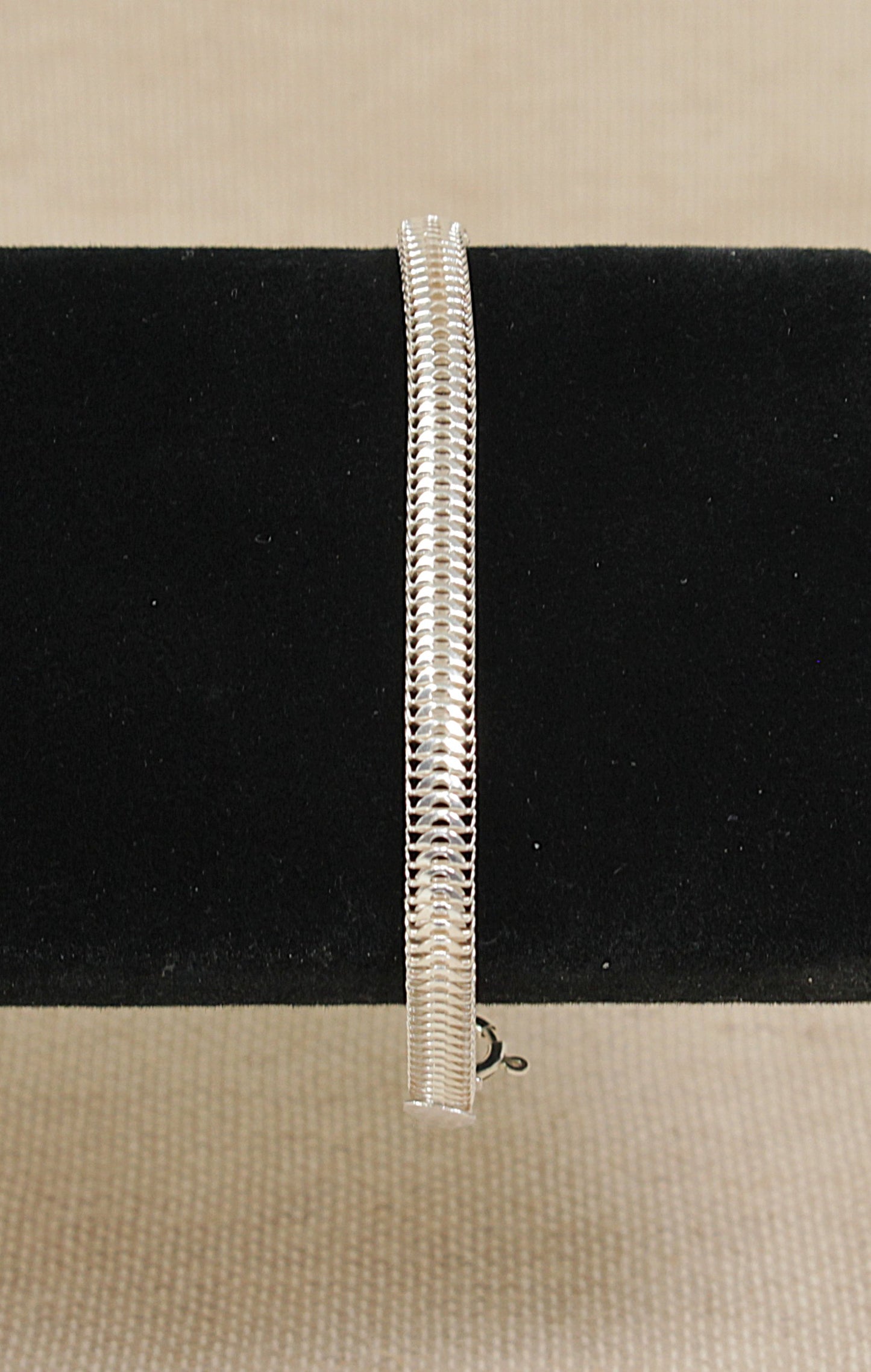 Silver snake chain bracelet on a black bracelet stand on a beige background 
