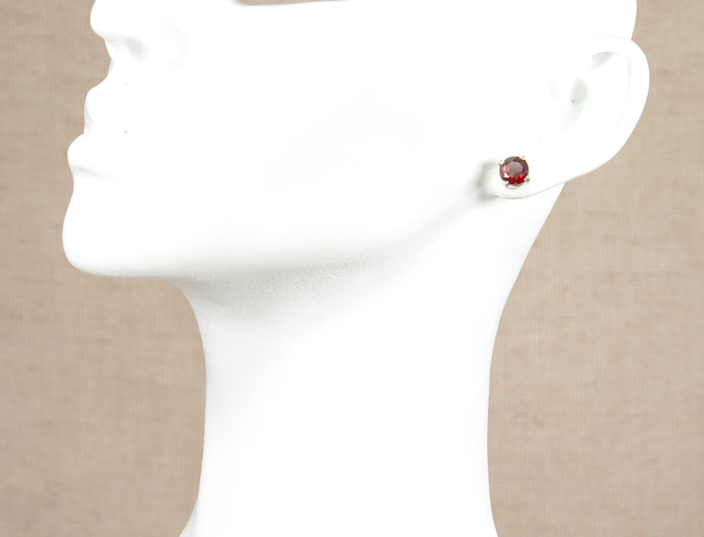 Close-up of a person wearing a silver  earring with a red garnet gemstone on a beige background