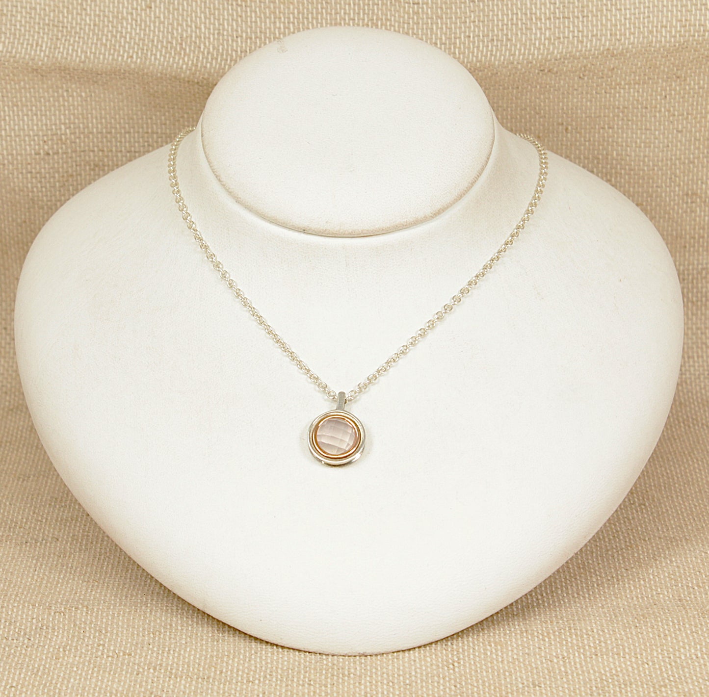 Welsh Clogau designer Necklace with a round gold and silver pendant on a white stand against a beige background