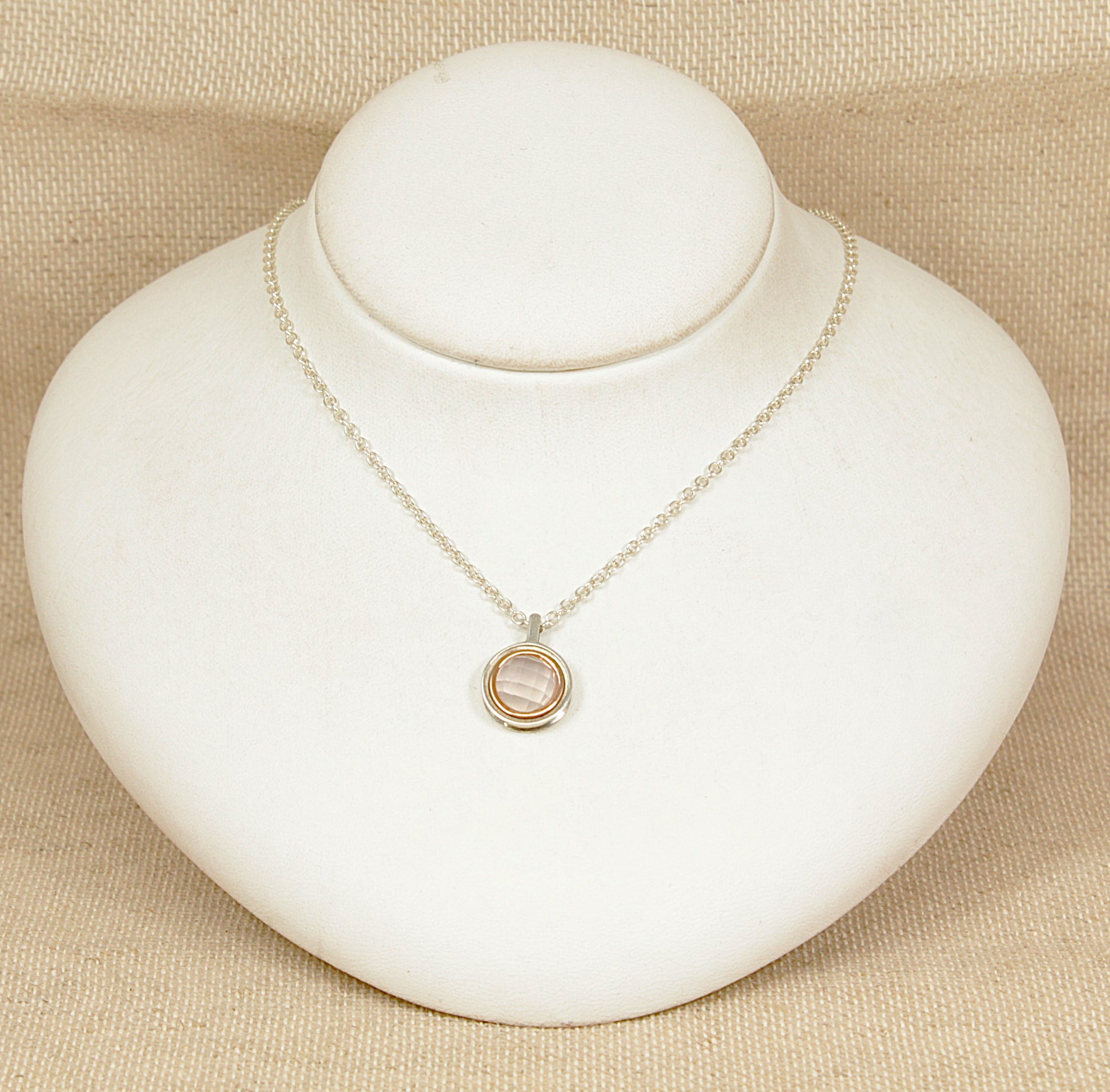 Welsh Clogau designer Necklace with a round gold and silver pendant on a white stand against a beige background
