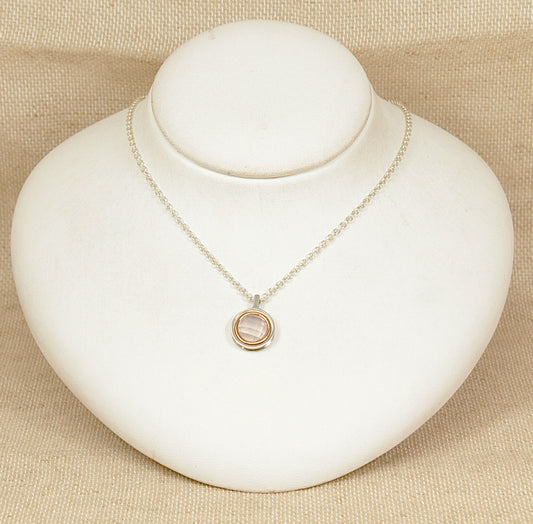 Welsh Clogau designer Necklace with a round gold and silver pendant on a white stand against a beige background