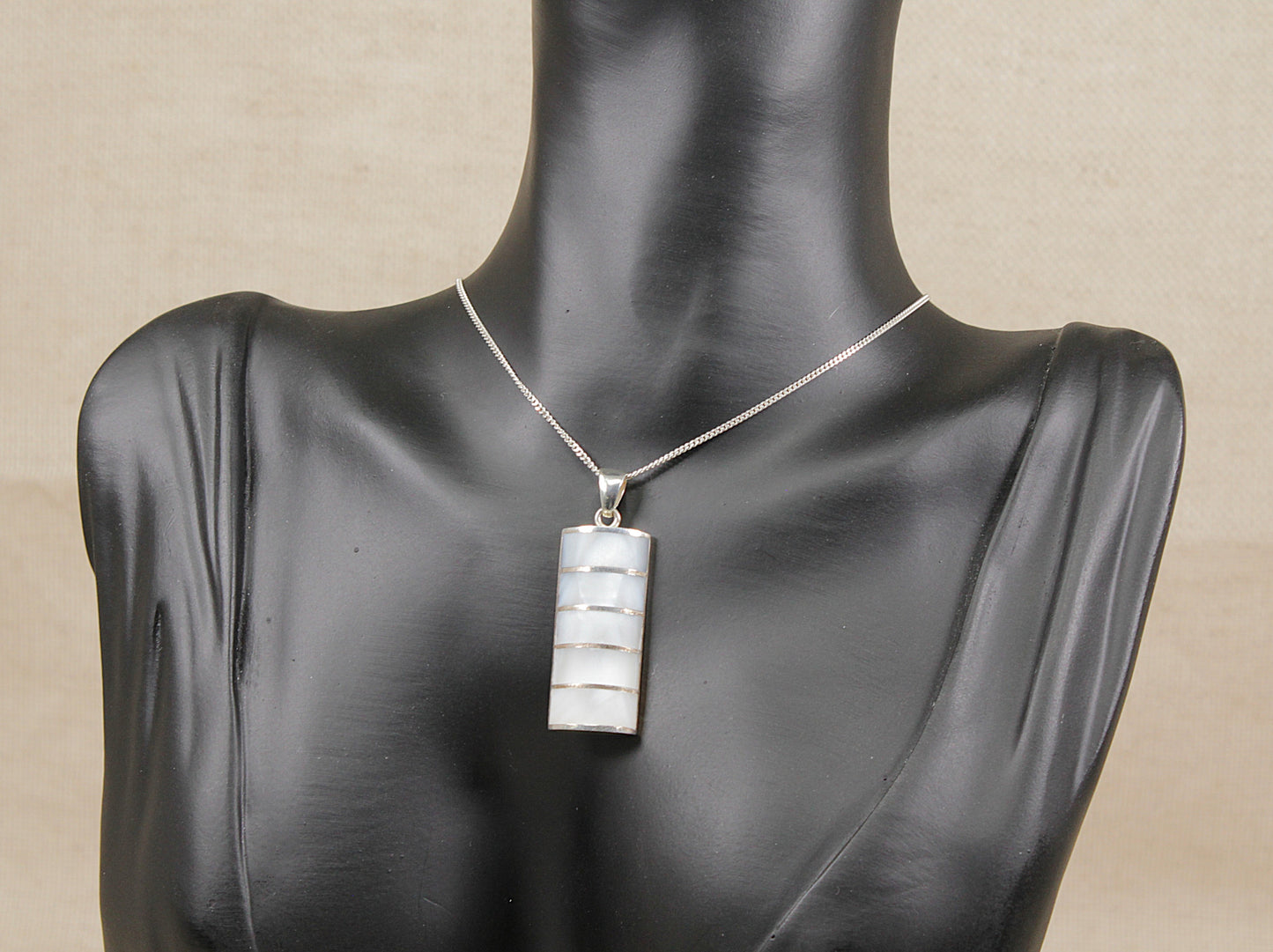 Mannequin wearing a silver necklace with a rectangular pendant on a beige background