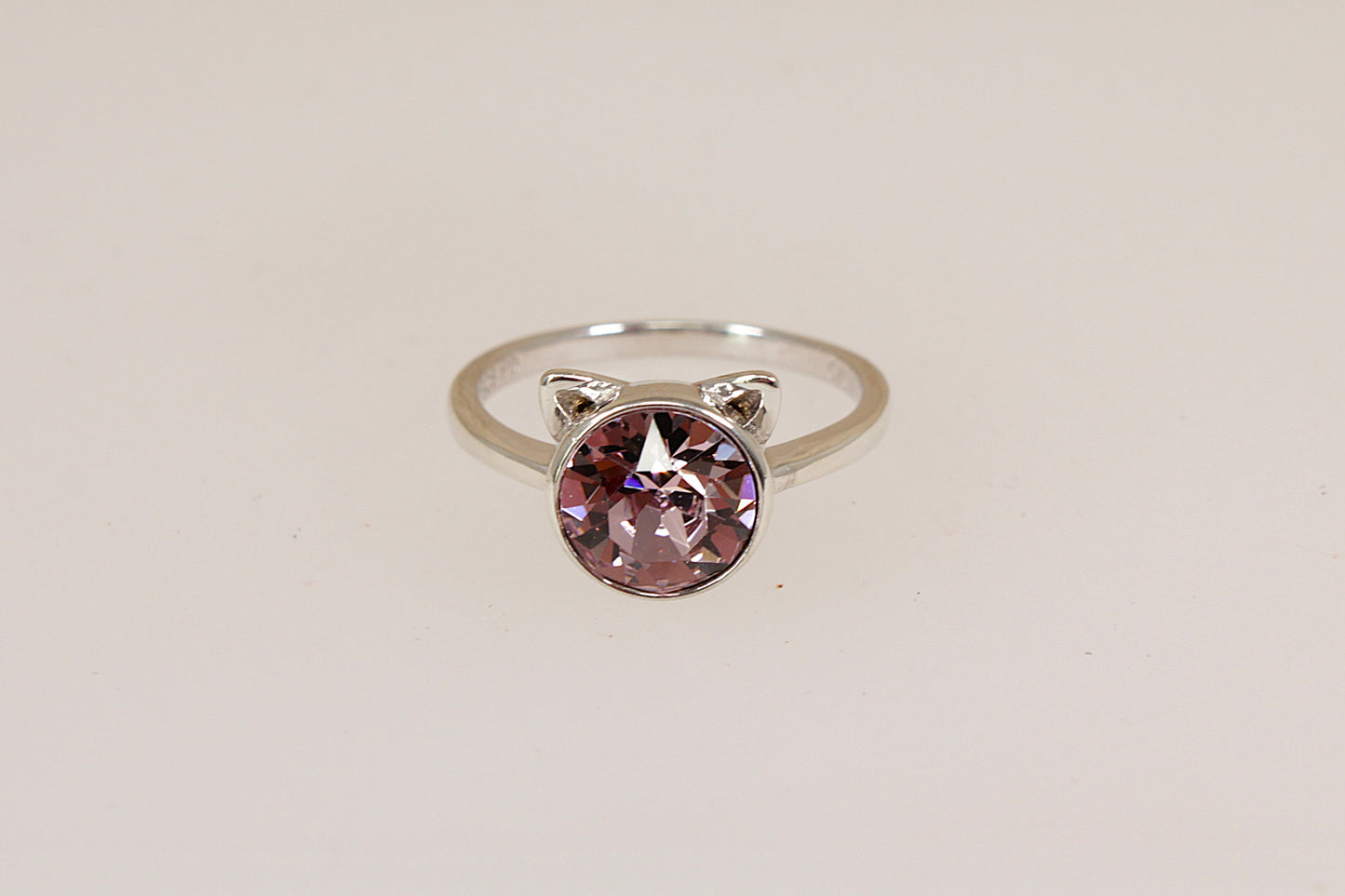 Silver ring with a pink gemstone and cats ears against a gray background