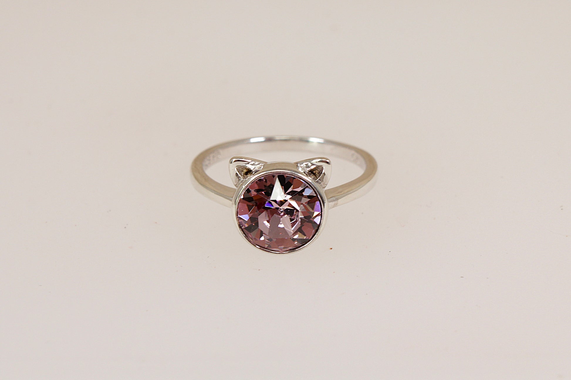 Silver ring with a pink gemstone and cats ears against a gray background