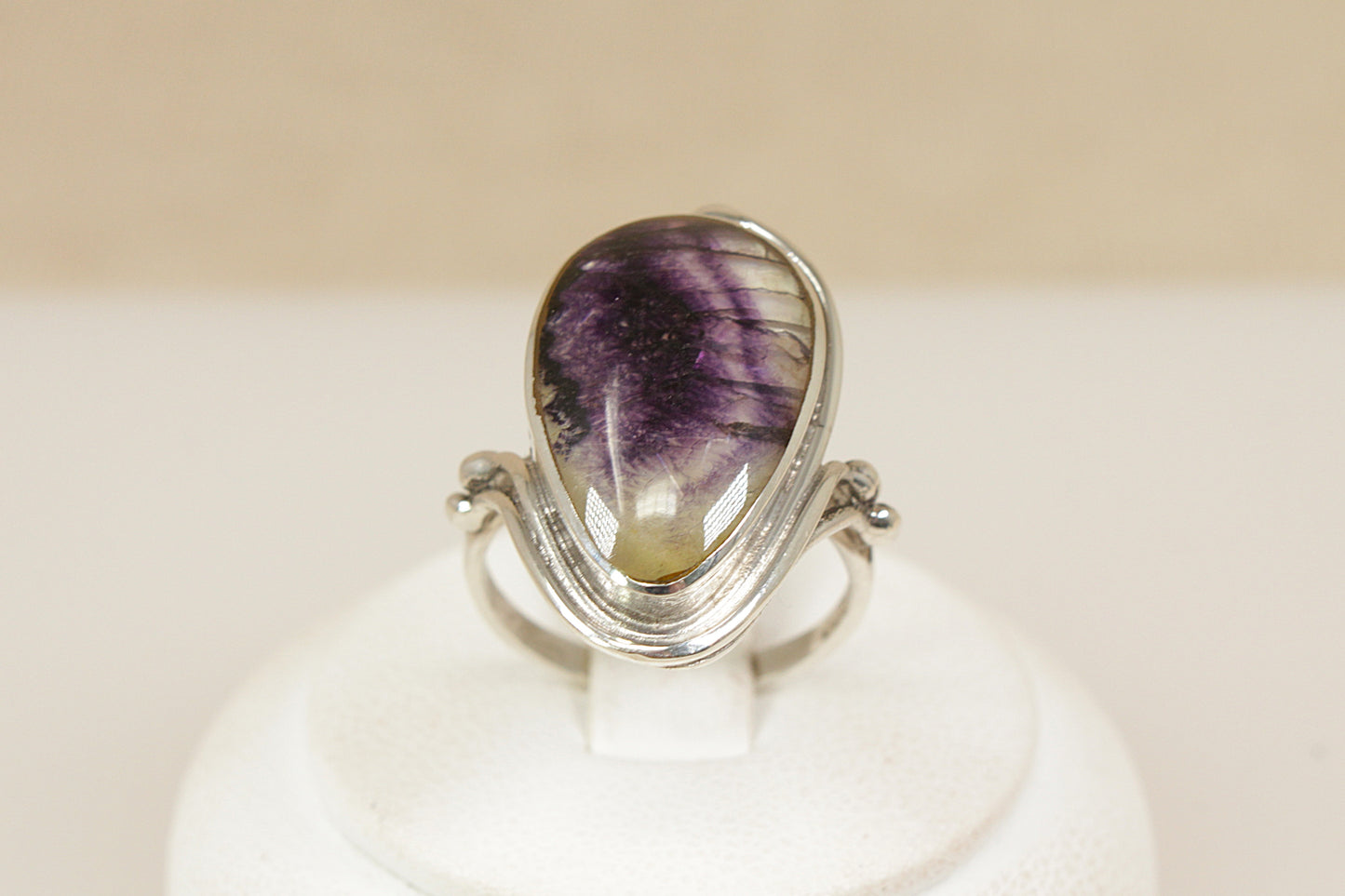 Derbyshire Blue John Statement Ring
A distinctive and beautifully designed sterling silver statement ring, showcasing a striking pear-shaped Blue John gemstone, bezel set to highlight its natural beauty, The silver mount features decorative Art Nouveau-inspired edging, with elegant curves and detailing that enhance the organic charm of the piece, Sheffield hallmarks for 1998, Blue John is a rare gemstone and only found in Derbyshire England, uk finger size N.