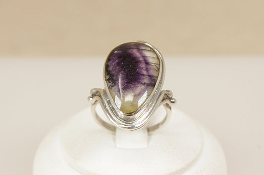 Derbyshire Blue John Statement Ring
A distinctive and beautifully designed sterling silver statement ring, showcasing a striking pear-shaped Blue John gemstone, bezel set to highlight its natural beauty, The silver mount features decorative Art Nouveau-inspired edging, with elegant curves and detailing that enhance the organic charm of the piece, Sheffield hallmarks for 1998, Blue John is a rare gemstone and only found in Derbyshire England, uk finger size N.