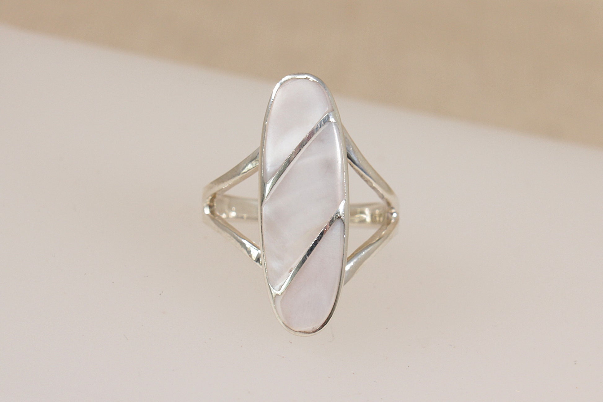 Silver ring with a geometric design of inset mother of pearl on a beige background