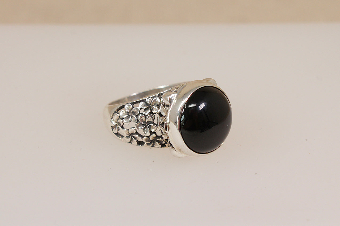 Silver Suarti statement ring with a dark garnet gemstone on a beige background
