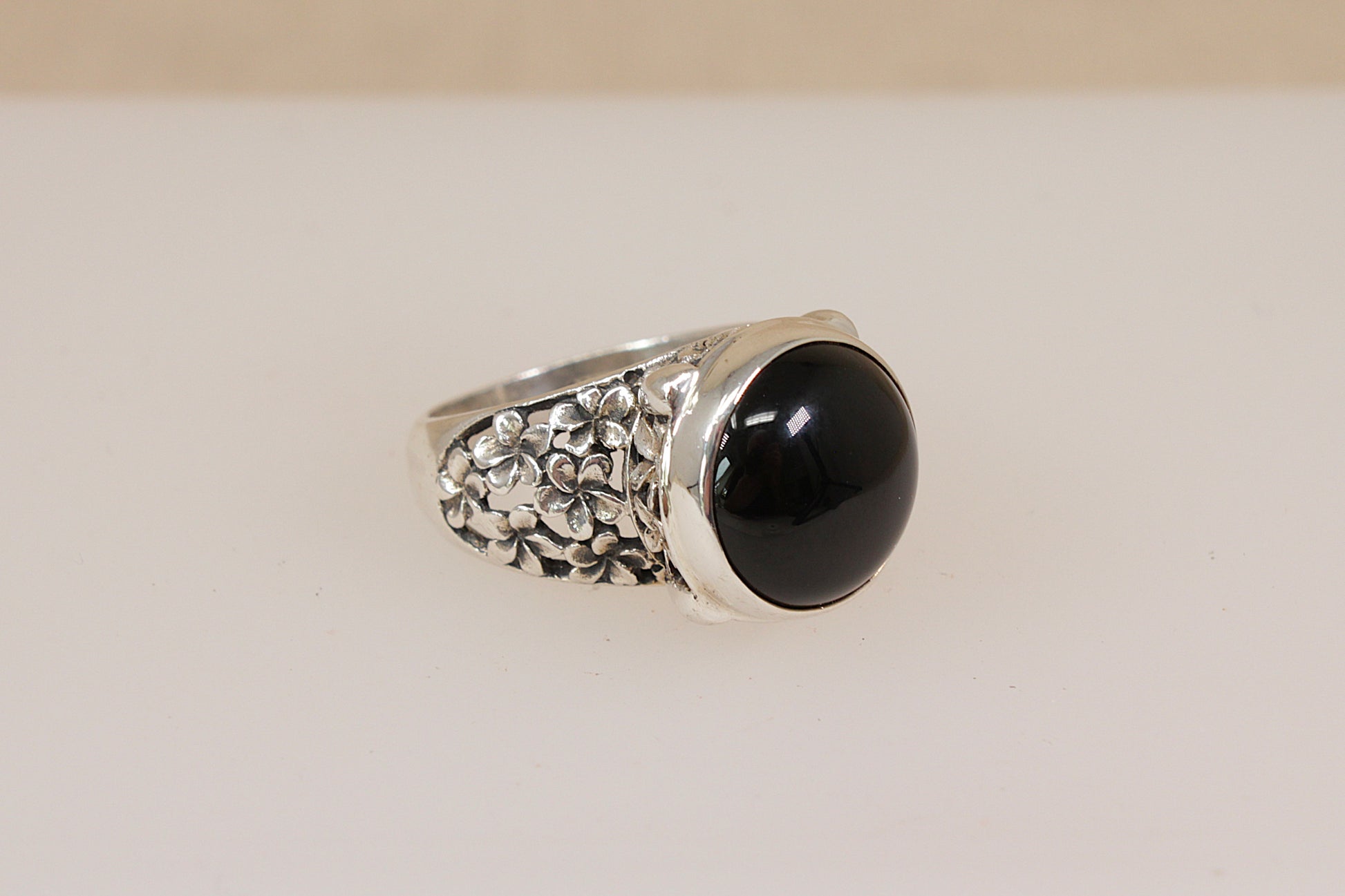 Silver Suarti statement ring with a dark garnet gemstone on a beige background