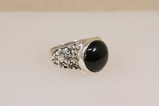 Silver Suarti statement ring with a dark garnet gemstone on a beige background